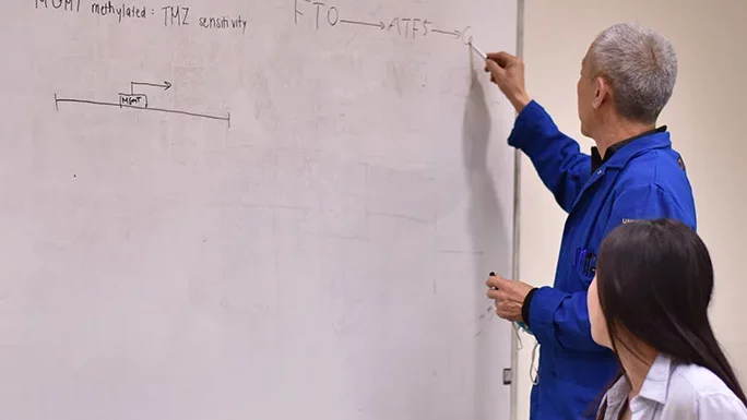 A Lai Lab member writes on a dry erase board while other members watch.