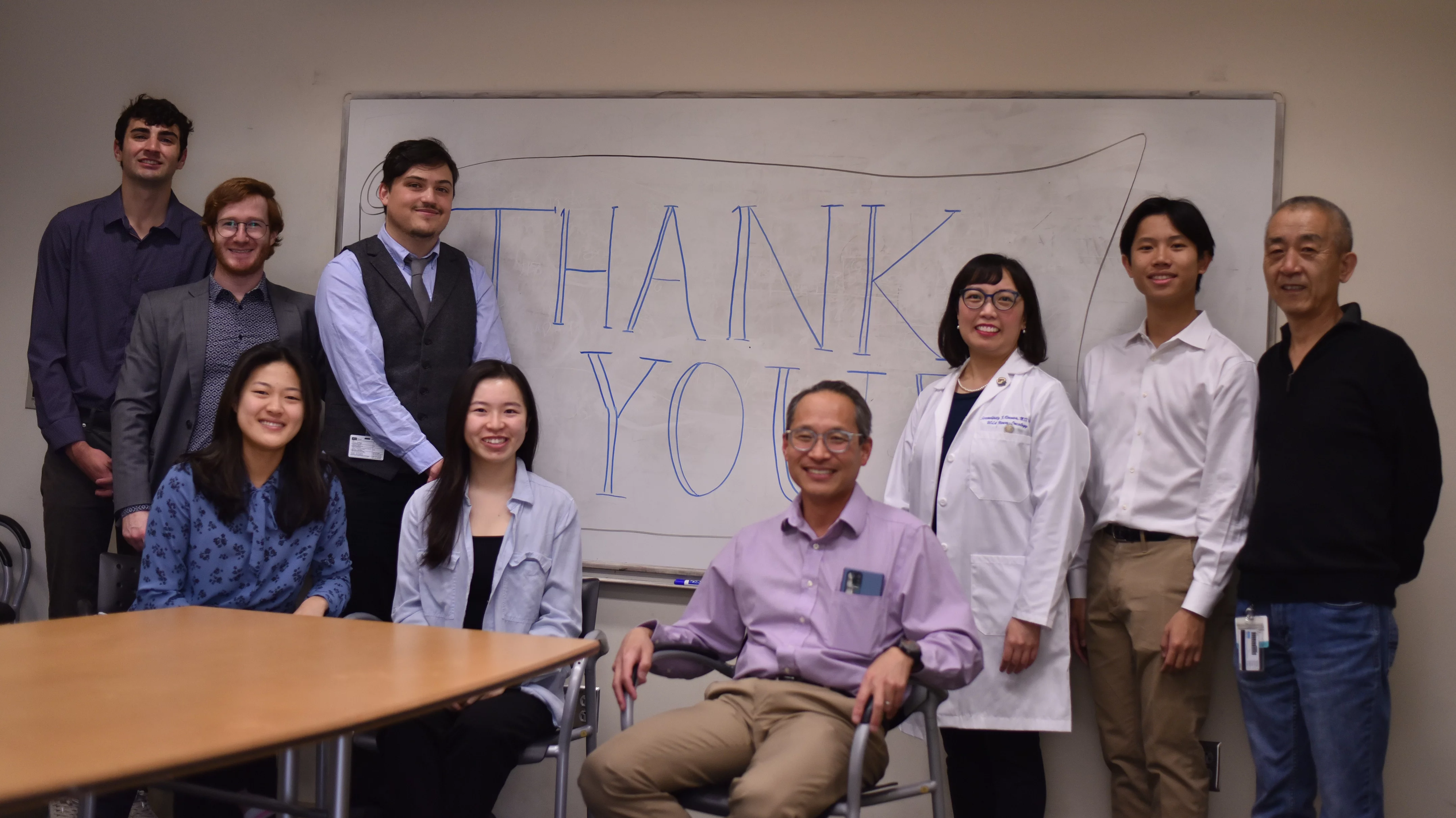 Lai lab members stand and sit at a table. A dry erase board behind them says "Thank you."